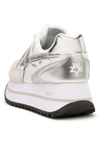 Sneaker argento e bianco con tomaia testurizzata, dettagli metallici, design a stella e suola bianca spessa con un motivo di battistrada nero.