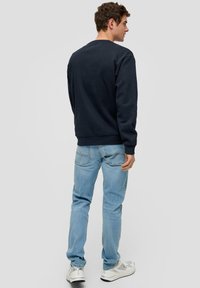 FELPA NAVY con scollo a giro e polsini a costine, abbinata a jeans azzurri chiari e sneaker bianche, vista da dietro.