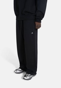 Svarte joggebukser med løs passform, med en liten hvit logo. Kombinert med metallisk sølvfargede sneakers, som fremhever designet og teksturen.
