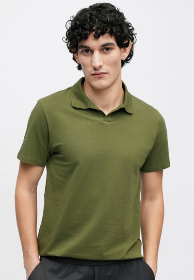 Olivzaļš polo krekls, izgatavots no gludas, vieglas auduma, ar klasisku apkakli un īsām piedurknēm, kopā ar pelēkām biksēm.