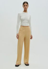 Witte, gestructureerde top met lange mouwen, gecombineerd met hooggewassen, wijde beige broeken, gedragen met zwarte plateausandalen. Eenvoudig, modern ontwerp.