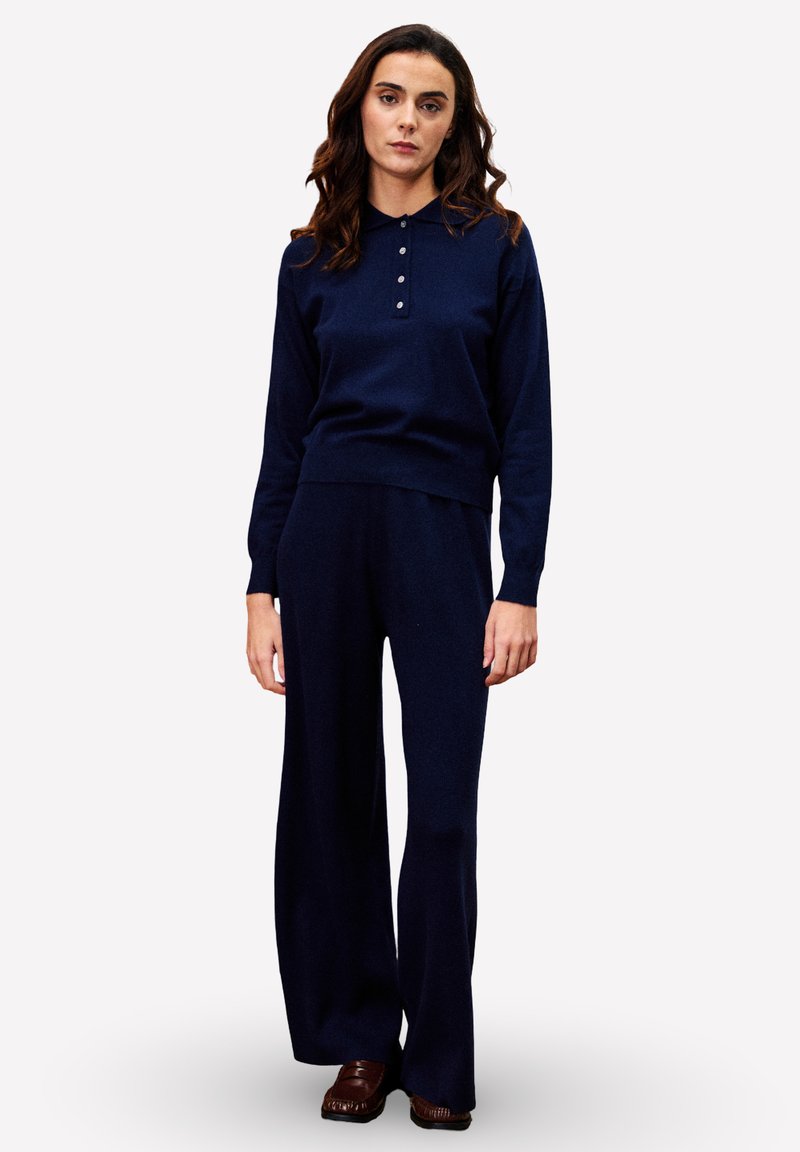 Ensemble de vêtements de détente en tricot marine comprenant un haut à col avec des accents de boutons et un pantalon à jambes larges. Texture douce et coupe décontractée dans l'ensemble.