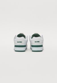 White sneakers with green accents, featuring a padded collar, logo on the heel, and a textured sole for grip. Clean, modern design.