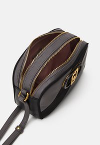 Sac à main en cuir avec deux compartiments zippés. Présente un extérieur noir, des détails gris et des accents en matériel doré. Texture lisse.