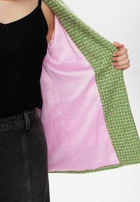 Grön och vit rutiga jacka med en rosa satinfoder, med en texturerad utsida och en slät insida. Inga synliga knäppningar.