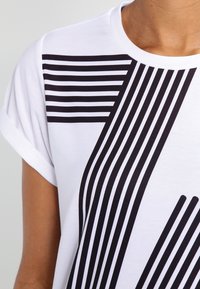 Hvid t-shirt med sort stribet grafisk design, der har forskellige tykkelser og vinkler. Blødt stof med optrukkede ærmer.