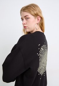 Felpa nera oversize con scollo rotondo, caratterizzata da un design testurizzato e con perline sulla parte posteriore in un motivo sparso.