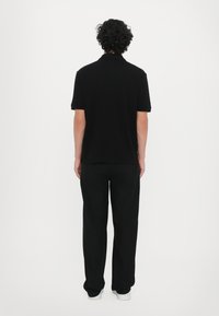 Svart polo skjorte med korte ermer, kombinert med svarte bukser og hvite joggesko. Glatt tekstur, klassisk design. Utsikt fra baksiden.