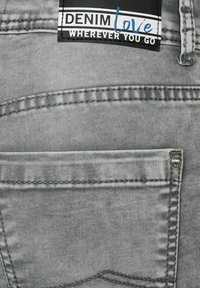 Grey denim jeans rear pocket with a black and white label reading "DENIM love WHEREVER YOU GO" stitched above the pocket.