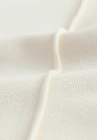 Kremo spalvos audinys su minkšta, lygiu tekstūra, matomas smulkus brūkšninimas ir šiek tiek blizgesio, sulankstytas sluoksniuotam efektui.