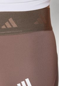 Leggice s teksturiranim smešnim pojasom u smešnoj boji, koje imaju tri dijagonalne pruge i glatko smešno telo, ukrašene belim logotipom na kuku.