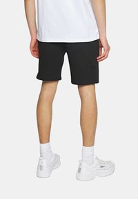Pantaloni neri realizzati in tessuto morbido, design lungo fino al ginocchio, caratterizzati da un orlo pulito. Abbinati a sneaker bianche e calze alla caviglia.
