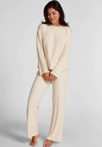Beige loungewear-set bestaande uit een top met lange mouwen en rechte pijpen. Gemaakt van zacht materiaal met een comfortabele pasvorm en minimalistisch ontwerp.
