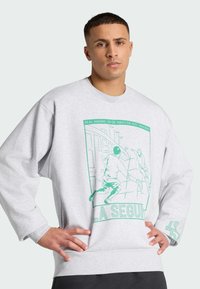 Sudadera gris con un diseño gráfico verde que muestra dos figuras. El diseño incluye texto y tiene un ajuste relajado y holgado.
