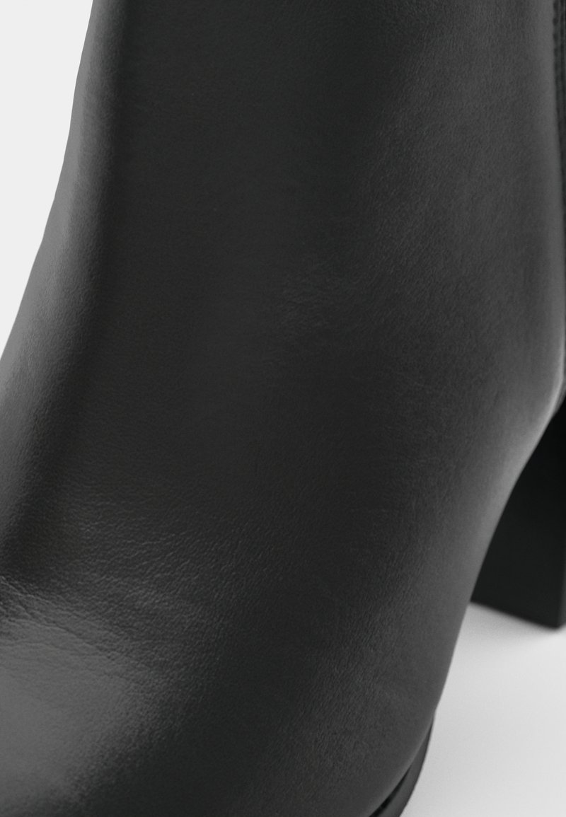 Schwarze Leder-Stiefelette mit glatter Textur, abgerundeter Zehenpartie und Blockabsatz. Fokus auf schickes Design und minimalistischen Stil.