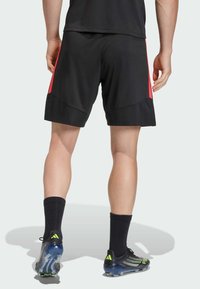 Čierne atletické šortky s červenými bočnými akcentmi, hladkou tkaninou a funkčným dizajnom. Čierne atletické ponožky a kopačky dopĺňajú vzhľad.