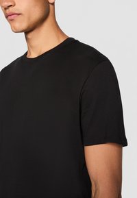 Camiseta de algodón negra de manga corta con cuello redondo y textura suave, con costuras visibles en las mangas y el dobladillo.