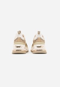 Baskets de sport beige et blanches au design épais, avec des accents transparents et un marquage métallique sur le talon et la semelle. Tige texturée.