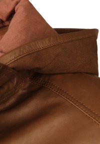 Brun läderjacka med en texturerad yta, som har en kontrasterande mjuk rosa tygfoder och synliga sömnadsdetaljer på kragen.