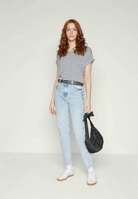 Striped t-shirt with rolled sleeves, light blue high-waisted jeans, black belt, and a black bag. White sneakers complete the look.