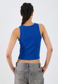 Afgemaakte mouwloze top in helderblauwe geribbelde stof. Ronde halslijn, gladde textuur. Draag met lichtgrijze high-waisted jeans.