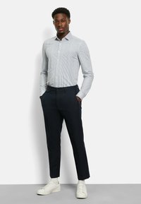 Herrenhemd in hellblau mit Streifen, dunkelblaue Hose und weiße Sneakers. Das Hemd hat einen Kragen und lange Ärmel. Die Hose ist tailliert und hat einen schlanken Schnitt.