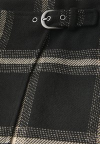 Zwarte en beige geruite stof met een zachte textuur heeft een zilveren gesp en oogjesdetail op een riem.