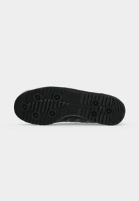 Μαύρη σόλα παπουτσιού Adidas με κυκλικά ανυψωμένα πέλματα και ανάγλυφο λογότυπο Adidas στο κέντρο, εμφανιζόμενη σε λευκό φόντο.
