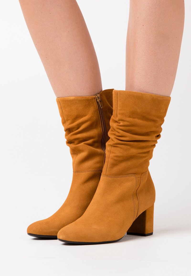 Bottines en cuir suede de couleur marron chaud, dotées d'un bout arrondi, d'un design froncé et d'un talon bloc. Détail de fermeture éclair sur le côté pour un enfilage facile.