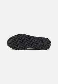 Sole di scarpa nera in gomma con un motivo a zig zag, con un'etichetta impressa al centro e un bordo liscio attorno al perimetro.
