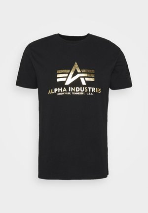 Tricou negru din bumbac cu un logo metalic auriu, având un design abstract și textul "ALPHA INDUSTRIES, KNOXVILLE, TENNESSEE, U.S.A."