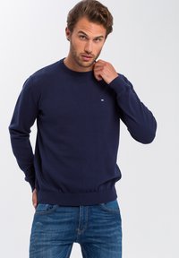 Granatowy sweter z długimi rękawami, okrągłym dekoltem, ściągaczami przy mankietach i w pasie. Mały szczegół z logo na piersi. Miękka, teksturowana tkanina.