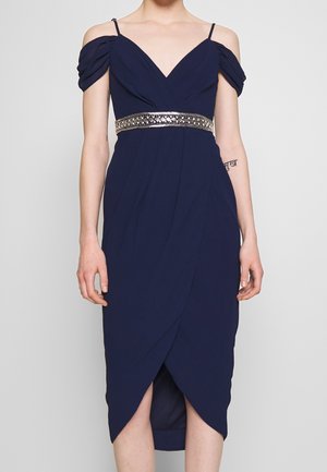 Robe bleu marine avec manches épaules dénudées, décolleté en V et ceinture ornée de détails métalliques. Comprend un design portefeuille et un ourlet mi-long.