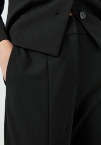 Černý oblek na míru s jedním knoflíkem, strukturovanou tkaninou a bočními kapsami, s elegantním, minimalistickým designem.