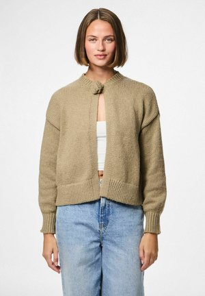 Beige gebreide cardigan met een ronde kraag, sluiting aan de voorkant met een decoratieve knoop, en geribde mouwen, gedragen over een witte top en blauwe jeans.