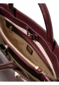 Sac à main en similicuir bordeaux avec un extérieur texturé, une quincaillerie dorée et un compartiment zippé à l'intérieur doté d'une doublure beige et d'un imprimé logo.