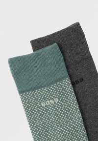 Dois pares de meias: um em cinza escuro e o outro em verde-azulado com uma bainha padrão apresentando gradientes verde-claro e branco, rotulado "BOSS".