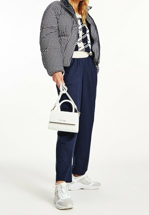 Kurtka puchowa w czarno-białą pepitkę, granatowe spodnie, biała torebka z fakturą oraz szare trampki z siateczkowymi detalami.