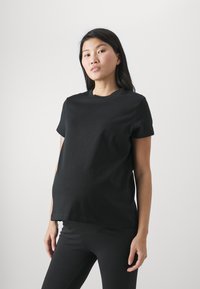 Zwart katoenen zwangerschapsshirt met korte mouwen, ronde halslijn en een losse fit, gedragen met zwarte leggings, gepresenteerd tegen een lichte achtergrond.