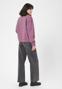 Felpa viola con polsini e orlo a coste, abbinata a jeans neri a vita alta con gamba larga e scarpe con piattaforma nera.