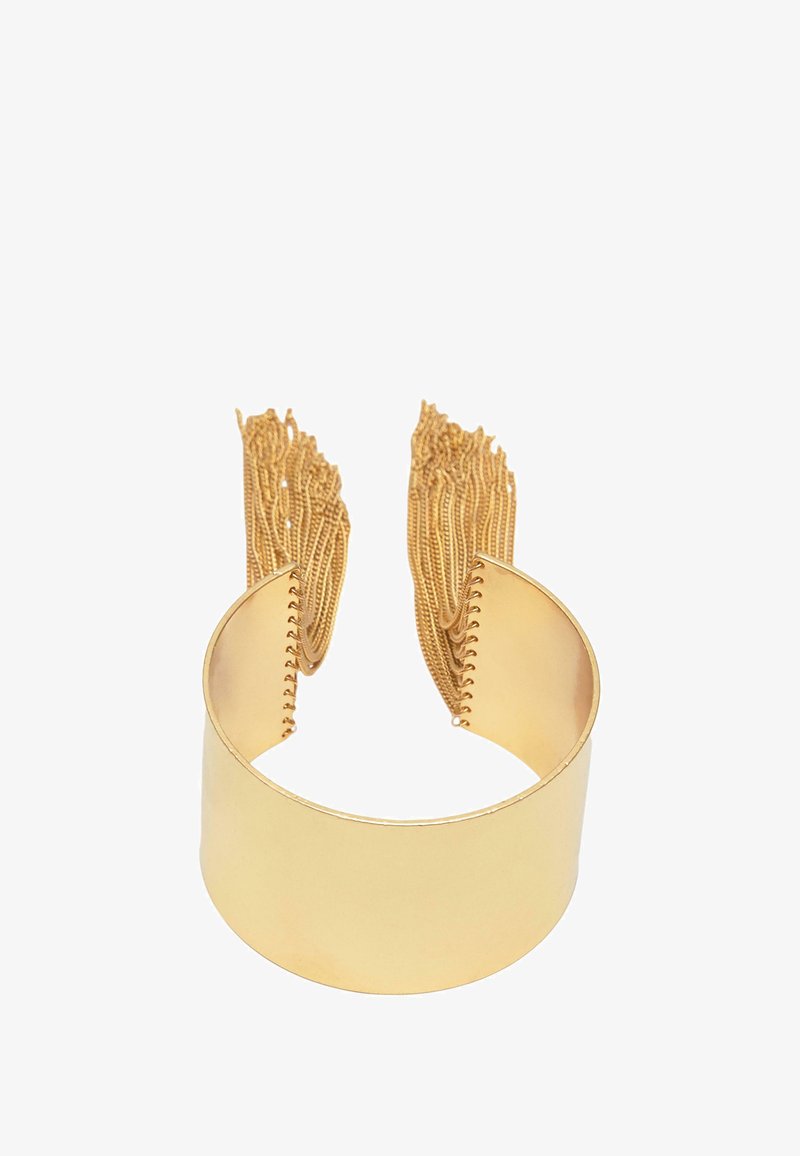 Kultainen panta rannekoru, jossa on sileä ja kiillotettu pinta. Seinillä roikkuvat frangipani-ketjut lisäävät tekstuuria ja ulottuvuutta. Yksinkertainen, avoin muotoilu.