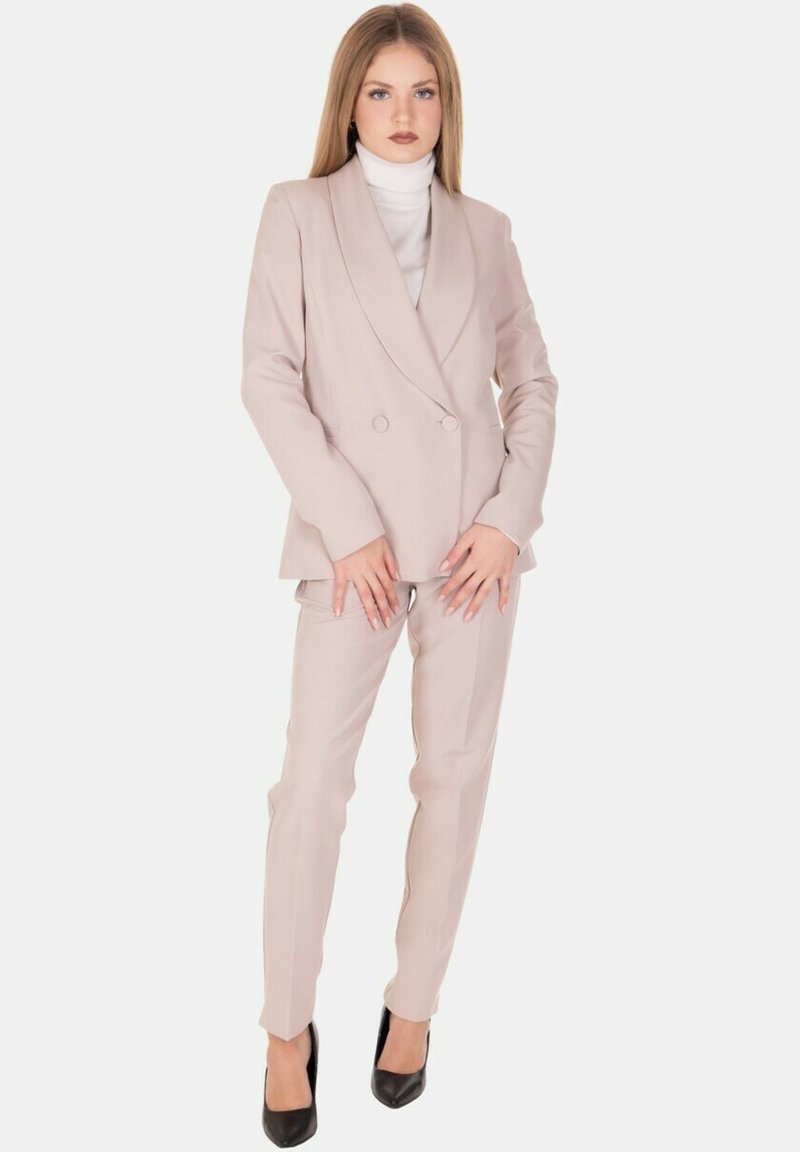 Completo sartoriale rosa chiaro composto da blazer doppiopetto e pantaloni aderenti, abbinato a un dolcevita bianco e tacchi neri.