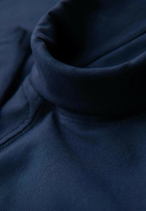 Tessuto blu navy con una consistenza morbida e un design con colletto alto. Le cuciture visibili lungo i bordi aggiungono dettaglio al capo.