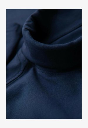 Tessuto blu navy con una consistenza morbida e un design con colletto alto. Le cuciture visibili lungo i bordi aggiungono dettaglio al capo.