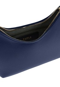 Borsa a mano in pelle blu navy con zip dorata parzialmente aperta, che mostra la fodera interna nera e l'etichetta del marchio Furla all'interno.
