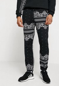 Černé tepláky s bílým vzorem paisley a malými puntíky. Mají elastický pás a boční pruhy. Vyrobeny z měkké, pružné látky.