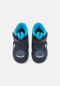 Botas para niño pequeñas de color azul marino con forro turquesa, exterior de tela, correas de velcro y suela de goma. Presentan costuras en contraste y un pequeño aplique.