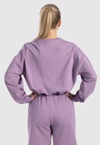 Felpa viola con una vestibilità comoda, dotata di maniche lunghe, polsini a costine e una vita elasticizzata. Tessuto liscio e morbido.