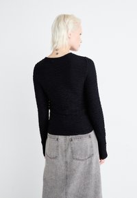 Svart langermet topp med en teksturert, krøllete design, med en avrundet halslinje. Kombinert med et grått denimskjørt.