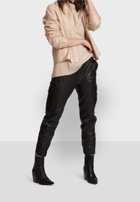 Beige linne skjorta med knappar lager på en ljusbeige topp, kombinerad med svarta läder cargo-byxor och spetsiga svarta klackboots.